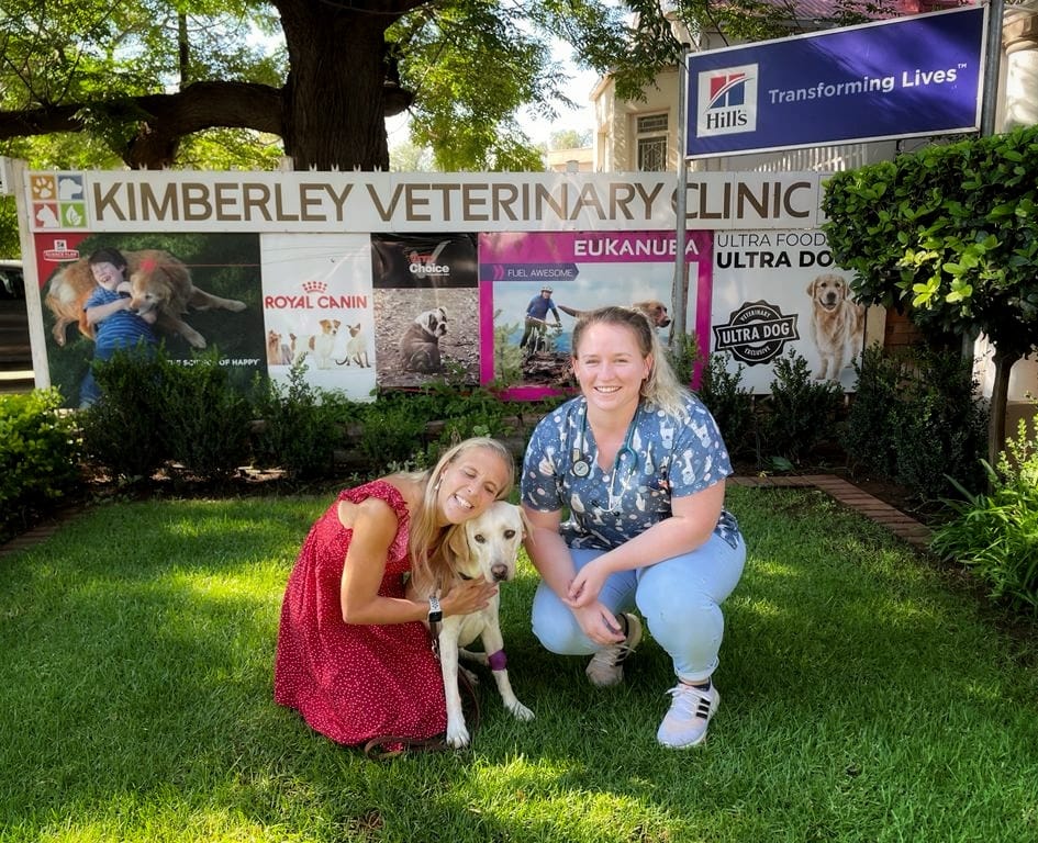 Blind owner with guide dog posing for photo with veterinarian in front of Kimberley Veterinary Clinic